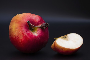 one whole red apple with a slice cut open on dark background