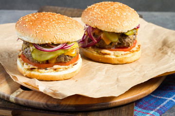 Fresh burger with beef on wooden table and paper. Gray background.