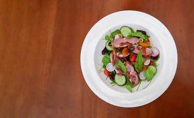 Smoked duck breast rocket salad orange balsamic vinaigrette in white ceramic plate on wooden background