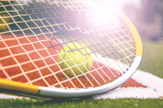 tennis ball and tennis racket on a tennis court with blurred background.