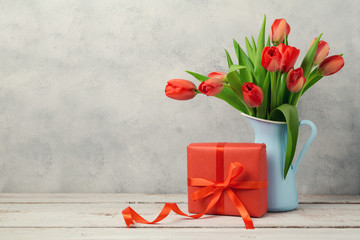 Red tulip flowers bouquet and gift box over rustic background. Women day or birthday celebration...