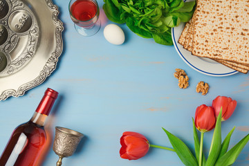 Passover holiday concept seder plate, matzoh, tulip flowers and wine bottle on wooden background. Top view from above