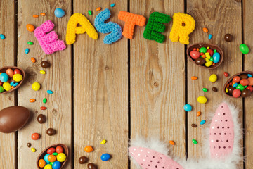 Obraz premium Easter holiday concept with chocolate eggs and bunny ears on wooden board background. Top view from above with copy space