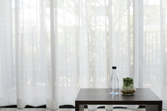 Office Desk With Bottle Of Water And Garden Plant On Glass Vase On White Drape Background Texture At Living Room.