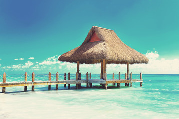 Tropical white sandy beach. Palm leaf roofed wooden pier with gazebo on the beach. Punta Cana, Dominican Republic. Instagram filter
