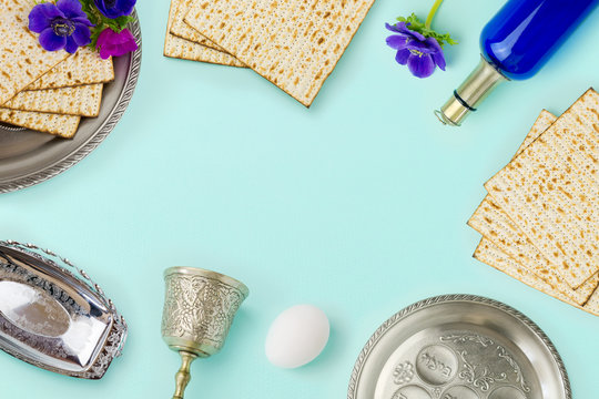 Passover holiday concept with wine bottle, matzoh and spring flowers over mint background with copy space. Top view from above