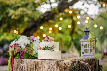 Beautiful wedding decoration with cake, bouquet of flowers and a lantern on a background of nature