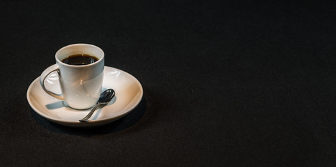 aromatic black coffee in a white cup, teaspoon, on a black background, drink set
