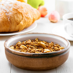 Oatmeal muesli with nuts, croissants, fruits, milk and coffee for delicious breakfast. Traditional healthy meal for breakfast on a table. Close-up.