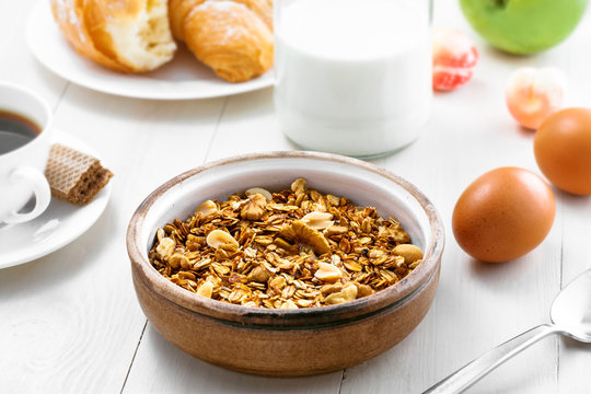 Oatmeal muesli with nuts, croissants, fruits, milk and coffee for delicious breakfast. Traditional healthy meal for breakfast on a table.