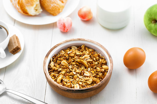 Healthy food for breakfast on a white wooden table. Oatmeal granola with nuts, coffee, croissants, eggs, milk and fruits for delicious healthy meal. Top view.