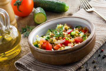 Healthy salad for breakfast made of couscous, tomatoes, cucumber and onion on a table. Traditional Israeli Ptitim meal. Moroccan cuisine food.
