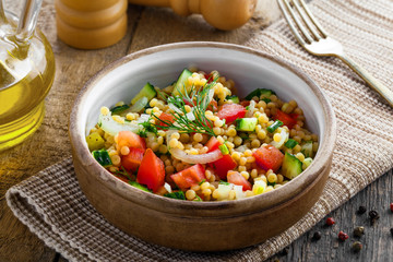 Couscous with tomatoes, cucumber and onion in a bowl for healthy breakfast. Traditional Israeli food Ptitim with vegetables. Moroccan cuisine meal.
