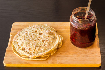 Pancake with silver spoon and red cranberry jam on a wooden board