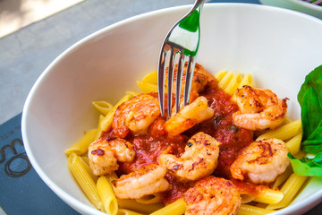 Fresh pasta with shrimp and tomato sauce with basil in a white bowl.