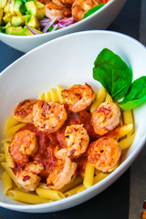 Fresh pasta with shrimp and tomato sauce with basil in a white bowl.