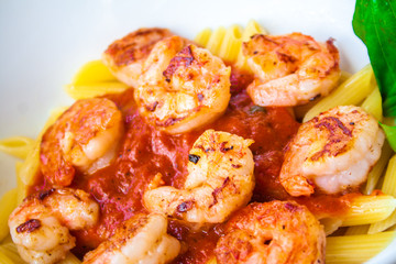 Fresh pasta with shrimp and tomato sauce with basil in a white bowl.