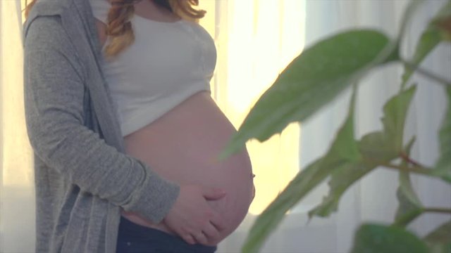 Pregnant happy woman holding blue baby shoes in her hands. Pregnancy concept. Slow motion 240 fps, 4K UHD video