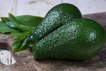 Green ripe avocado with leaves on granite plank