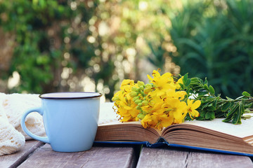 old book, cup of coffee next to field flowers
