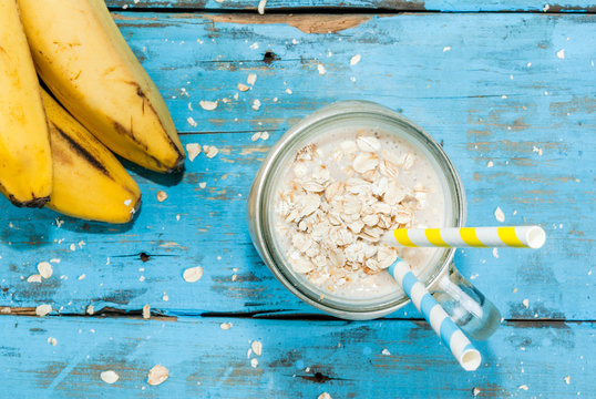 Smoothies with yogurt, banana and oatmeal in a mason jar. On light blue wooden table, with ingredients for cooking. Copy space