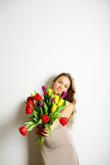 Smiling young woman in a beige dress holding a bouquet of bright colors