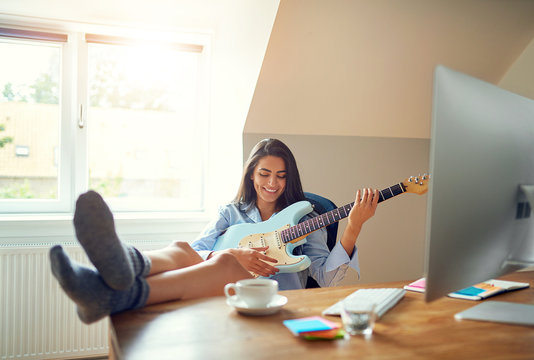 Cute woman playing guitar in front of computer