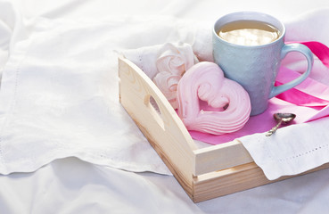 Fototapeta na wymiar A tray with a cup of hot tea and homemade meringue in the form of heart in a bed on a white textile