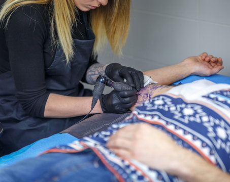 A tattoo artist woman draws with her tattoo machine, a tattoo on the arm of a man