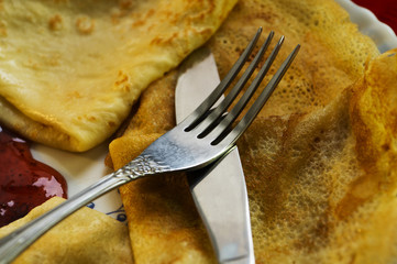 Pancakes with cherry jam and cutlery on a red background