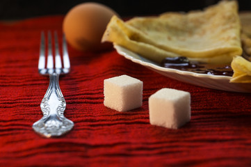 Pancakes with cherry jam, cutlery, sugar and eggs on a red background