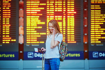 Tourist girl with backpack and carry on luggage in international airport, near flight information board