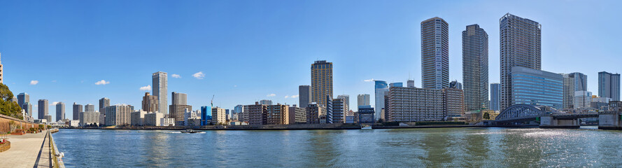 Wide angle panoramic view of winter Sumida river under blue sky in Tokyo with wavy water, boats, bridge and skyscrapers