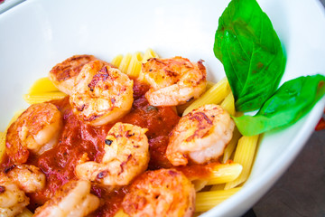 Fresh pasta with shrimp and tomato sauce with basil in a white bowl.