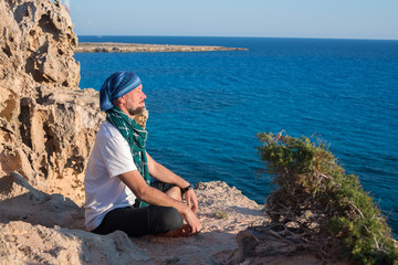 Bearded man traveler meditate and relax on a rocky seashore