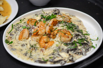 Fresh pasta with shrimp and tomato sauce with basil in a white bowl.