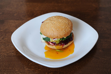 Burger with cutlet, vegetables, cheese and berry sauce closeup on a white plate on a wooden background