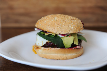 Burger with cutlet, vegetables, cheese and berry sauce closeup on a white plate on a wooden background