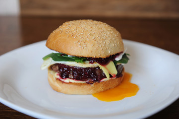 Burger with cutlet, vegetables, cheese and berry sauce closeup on a white plate on a wooden background