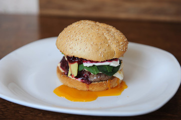 Burger with cutlet, vegetables, cheese and berry sauce closeup on a white plate on a wooden background