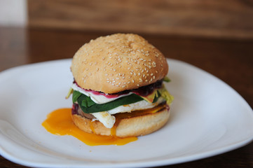 Burger with cutlet, vegetables, cheese and berry sauce closeup on a white plate on a wooden background