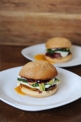 Burger with cutlet, vegetables, cheese and berry sauce closeup on a white plate on a wooden background