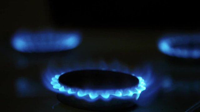 Cooktop with burning gas ring. Gas cooker with blue and yellow flames in dark.