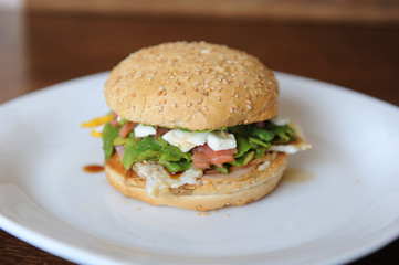 Burger with red fish, bacon, vegetables, cheese and berry sauce closeup on a white plate on a wooden background