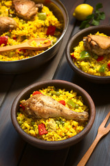Chicken paella, a traditional Valencian (Spanish) rice dish made of rice, chicken, peas and capsicum , photographed on dark wood with natural light (Selective Focus on the chicken thigh)