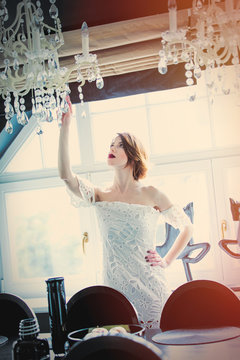 beautiful young woman standing near the table in the luxury room and touching chandelier