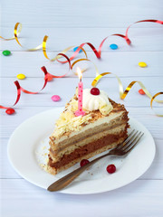 piece of chocolate banana cake decorated with rosettes of cream, berries and candles on light wooden background. Birthday.