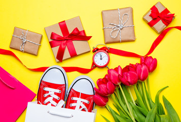 bunch of red tulips, red gumshoes, cool shopping bags, ribbon, alarm clock and beautiful gifts on the wonderful yellow background