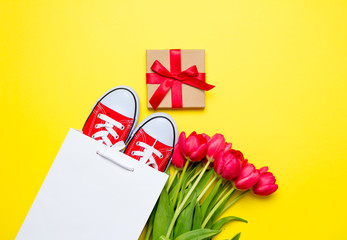 bunch of red tulips, red gumshoes, cool shopping bag and beautiful gift on the wonderful yellow...