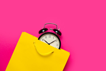 cool black alarm clock in beautiful yellow shopping bag on the wonderful pink background